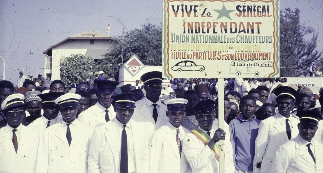 Nach der Unabhängigkeit afrikanischer Staaten öffneten sich zunächst neue Möglichkeiten. Organisierte Chauffeure drücken 1962 ihre Unterstützung für die Republik Senegal aus. Foto: Maarten van Dis/ NSAG (Nederlands studenten Afrika Gezelschap) (CC BY-SA 4.0) Männer in weißen Anzügen protestieren in Senegal