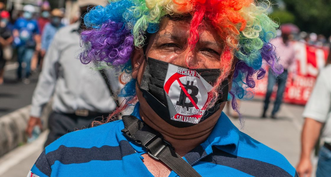 Nicht alle sind vom Bitcoin begeistert. In San Salvador sorgte die offizielle Einführung der Kryptowährung für Proteste. Foto: Guayo Fuentes/Shutterstock.com Mann mit Clownsperücke und Protestaufklebern auf seiner Kleidung