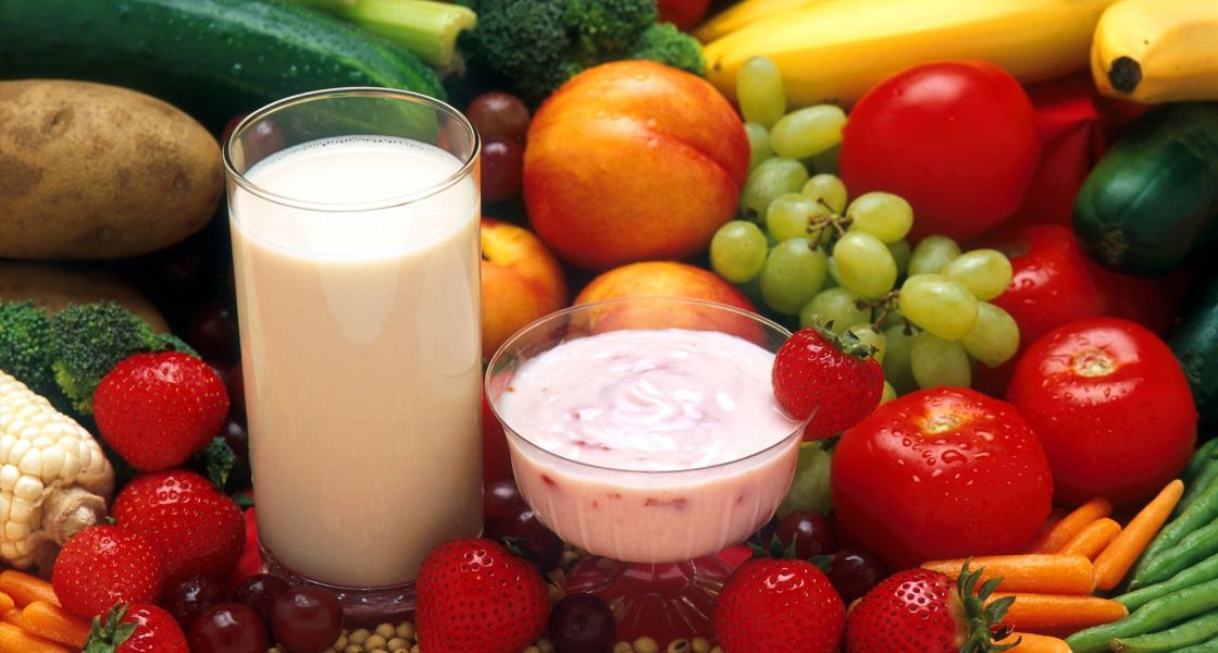 Frisches Obst und Gemüse, ein Milchglas, Joghurt und Kerne liegen dekorriert auf einem Tisch