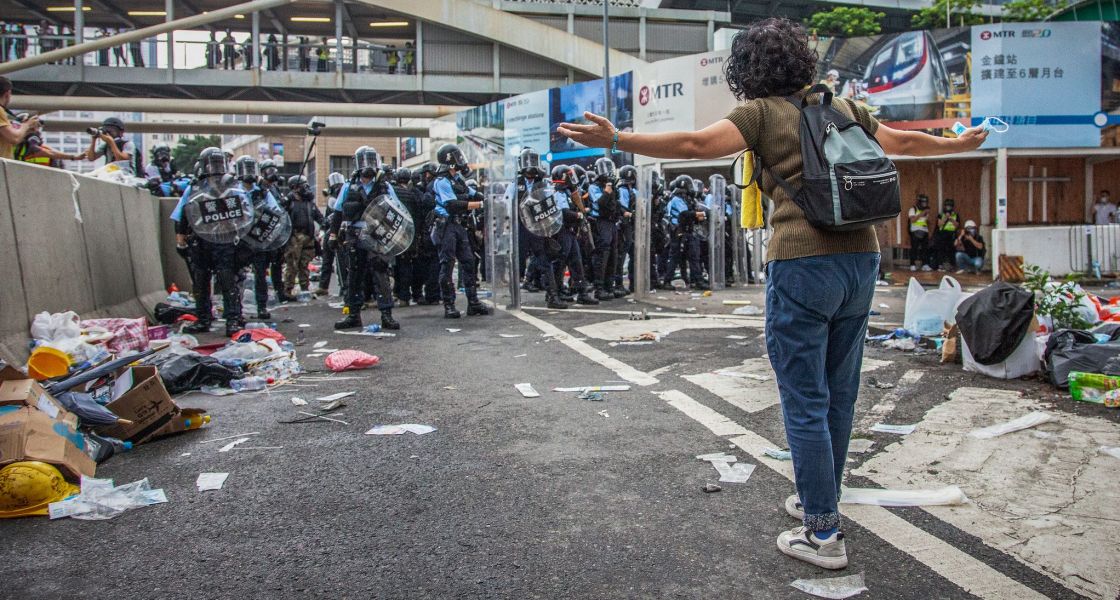 Eine Frau steht auf einer urbanen Straße, ihr gegenüber stehen Polizist*innen. | Studio Incendo (CC BY 2.0)