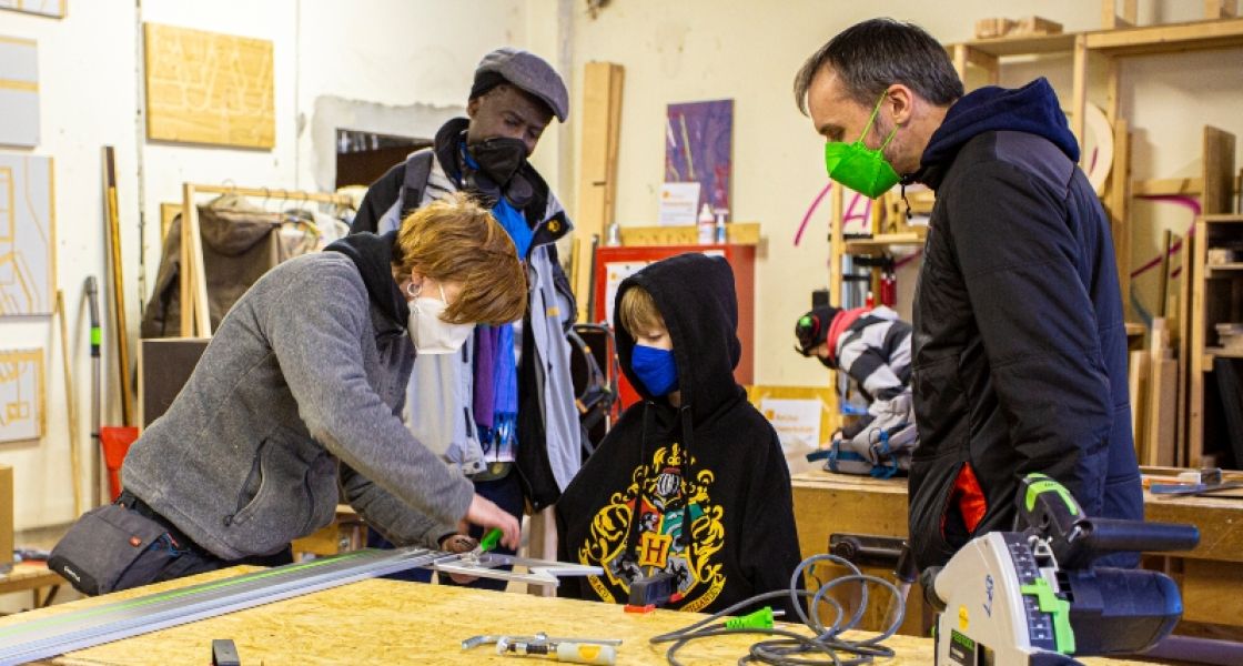 Aktionstag im Haus der Materialisierung, Berlin; Foto: Raquel Gomez Aktionstag im Haus der Materialisierung, Berlin; 4 Personen stehen an einer Werkbank, Copyright Raquel Gomez
