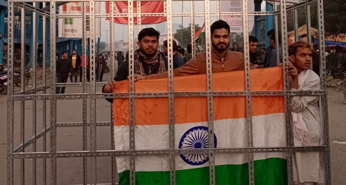 Eingesperrt: Der Spielraum für die indische Zivilgesellschaft wird kleiner, In Dehlis Statdviertel Shaheen Bagh war die Käfigaktion Teil wochenlanger Proteste (vor der COVID-Pandemie) Drei Personen mit der indischen Flagge in einem Kaäfig. Während eines Protest in Shaheen Bagh; Januar 2020