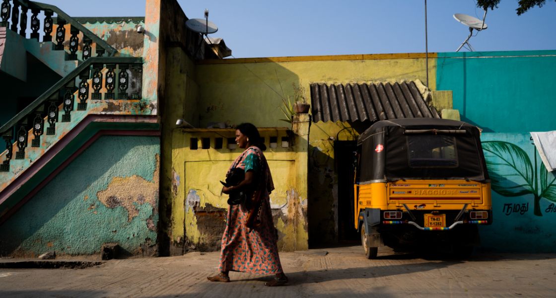 Heimarbeiterin in Indien, Ambur Eine Frau läuft die Straße entlang, unter dem Arm hat sie Material zum Schuhe-nähen