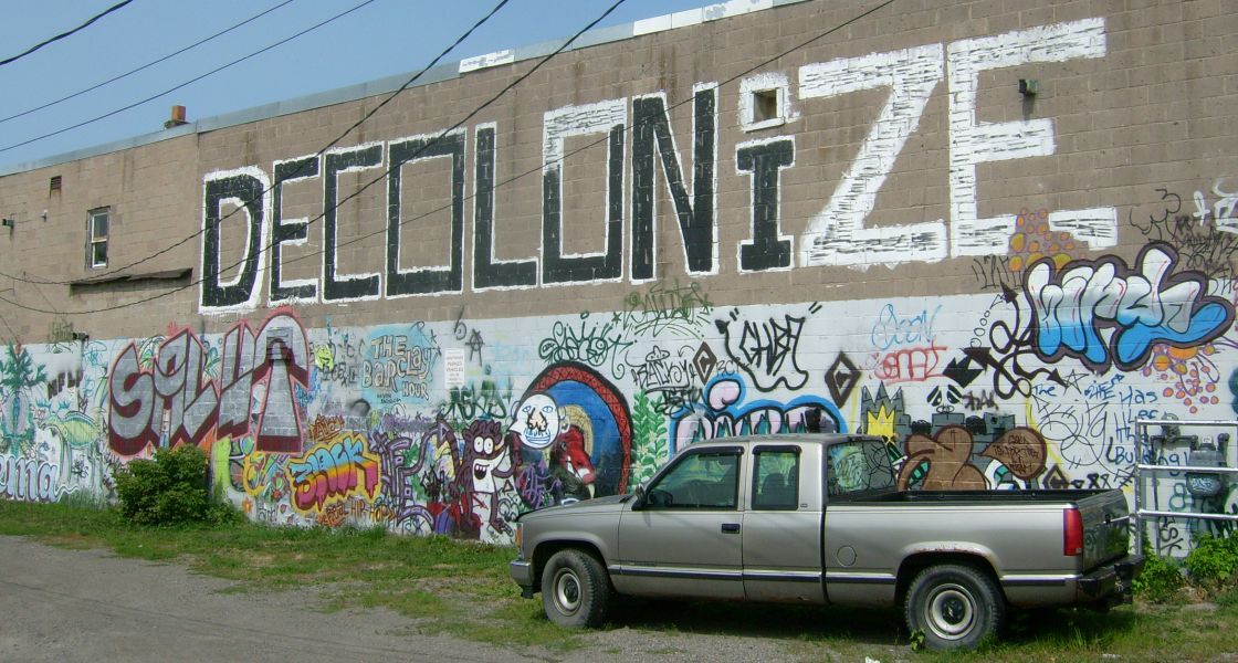 Eine mit Graffiti besprühte Wand zeigt groß den Schriftzug Decolonize Besprühte Wand mit Schriftzug Decolonize