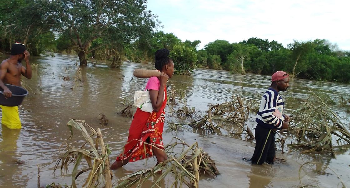 Menschen in Mosambik laufen knietief durch das Wasser eines überflutetetn Maisfeldes
