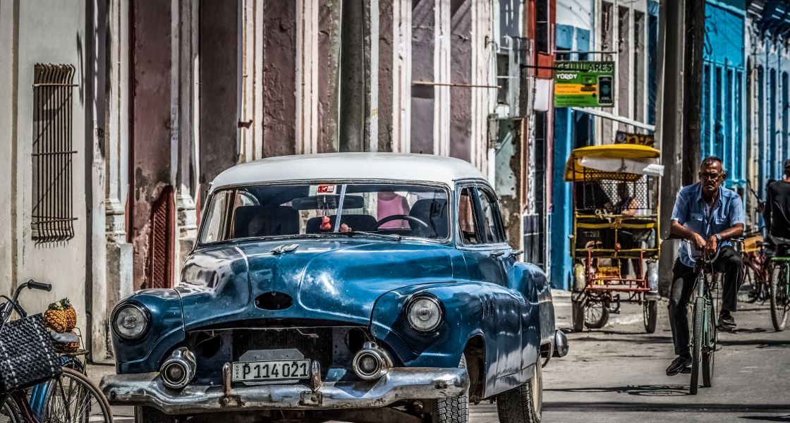 Eine Straßenszene in Kuba: ein Oldtimer und ein Mann auf dem Fahrrad