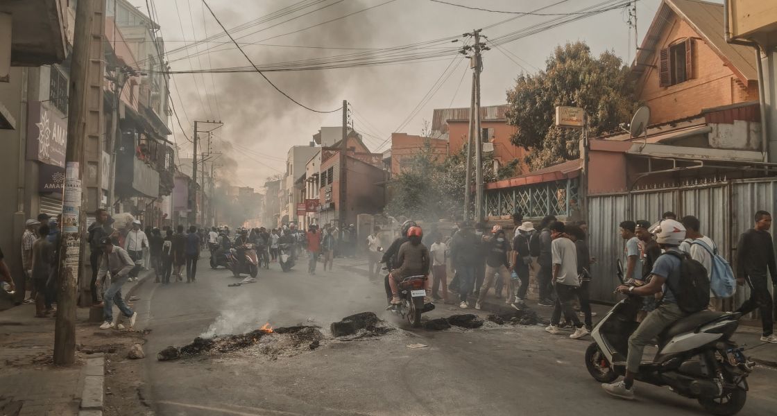 Foto einer brennenden Straßenblockade; viele junge Menschen auf der Straße