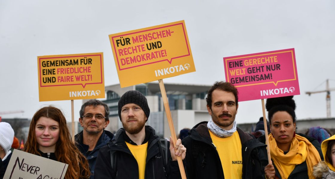 Eine Gruppe Menschen mit Schildern mit der Aufschrift "Gemeinsam für eine friedliche und faire Welt!", "Für Menschenrechte und Demokratie" und "Eine gerechte Welt geht nur gemeinsam, INKOTA" vor dem Kanzleramt