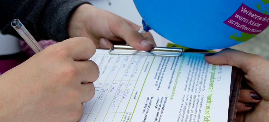 jemand schreibt auf einem Blatt Papier und daneben ein blauer Luftballon
