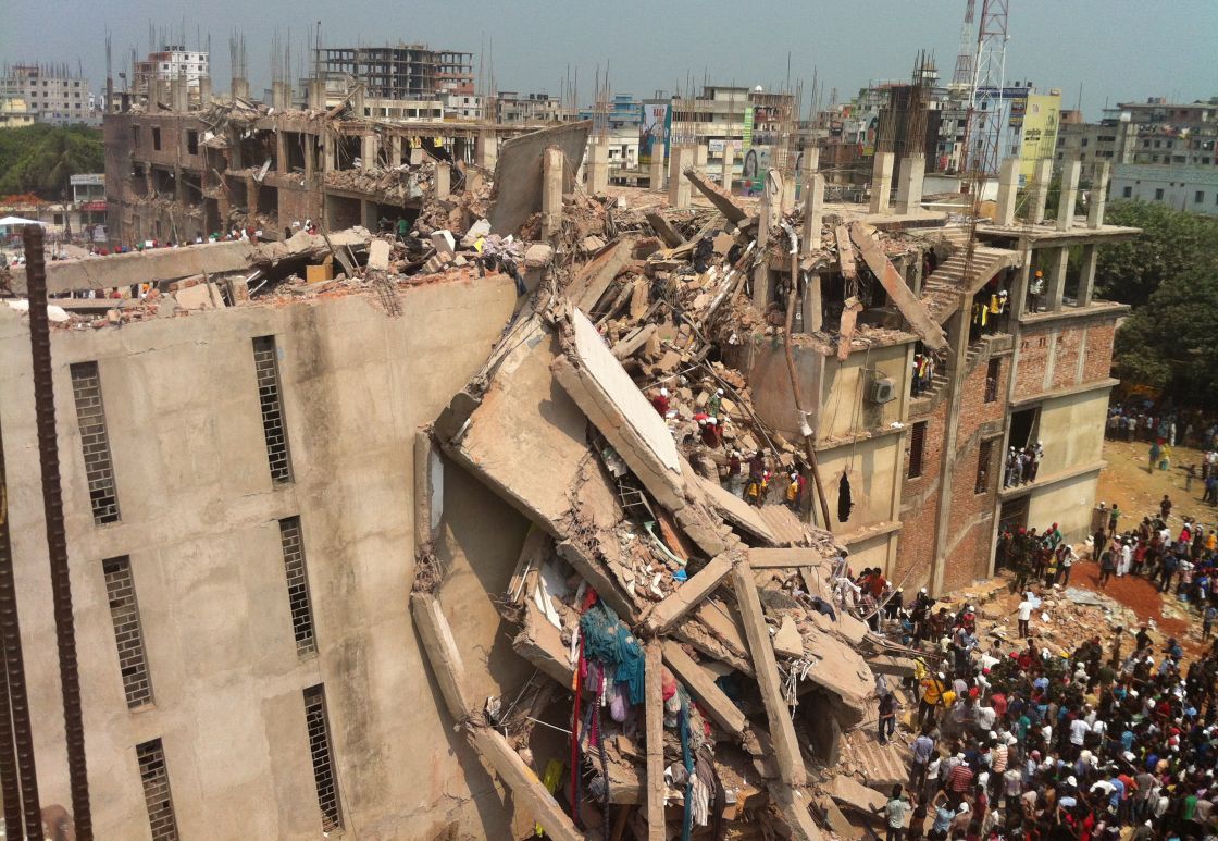 ein hohes Fabrikgebäude, was teilweise eingestürzt ist. Rettungskräfte sind in den Trümmern zu sehen