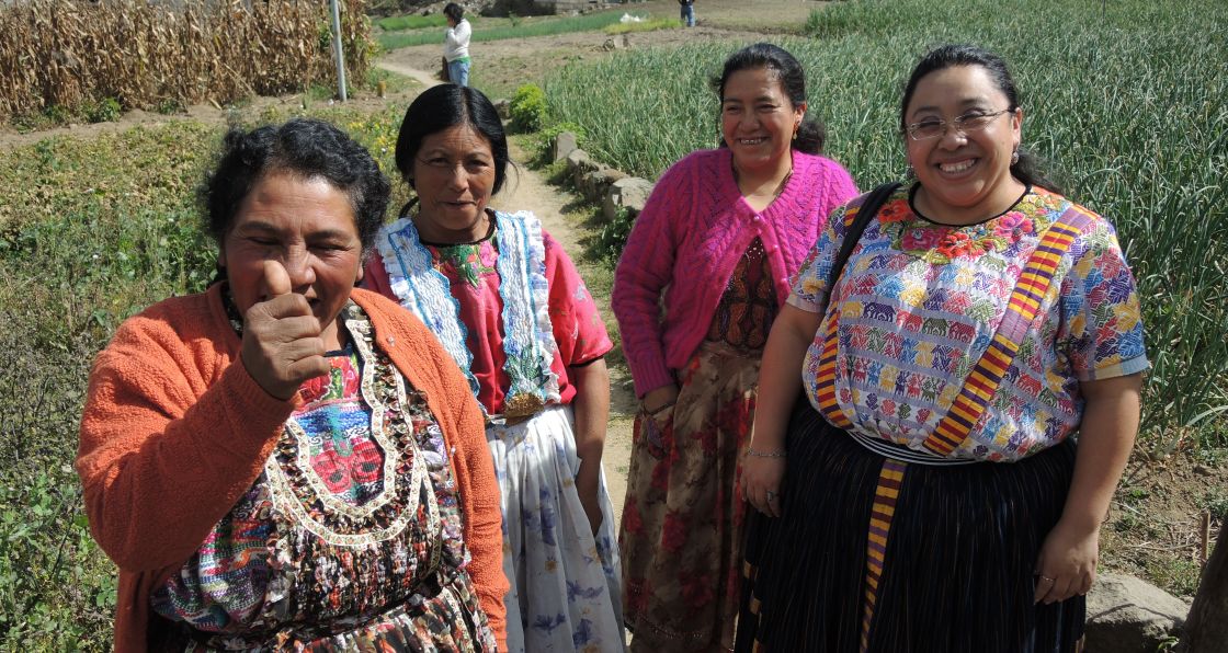 Vier gutgelaunte Frauen in traditionellen Kleidern stehen vor einem Feld