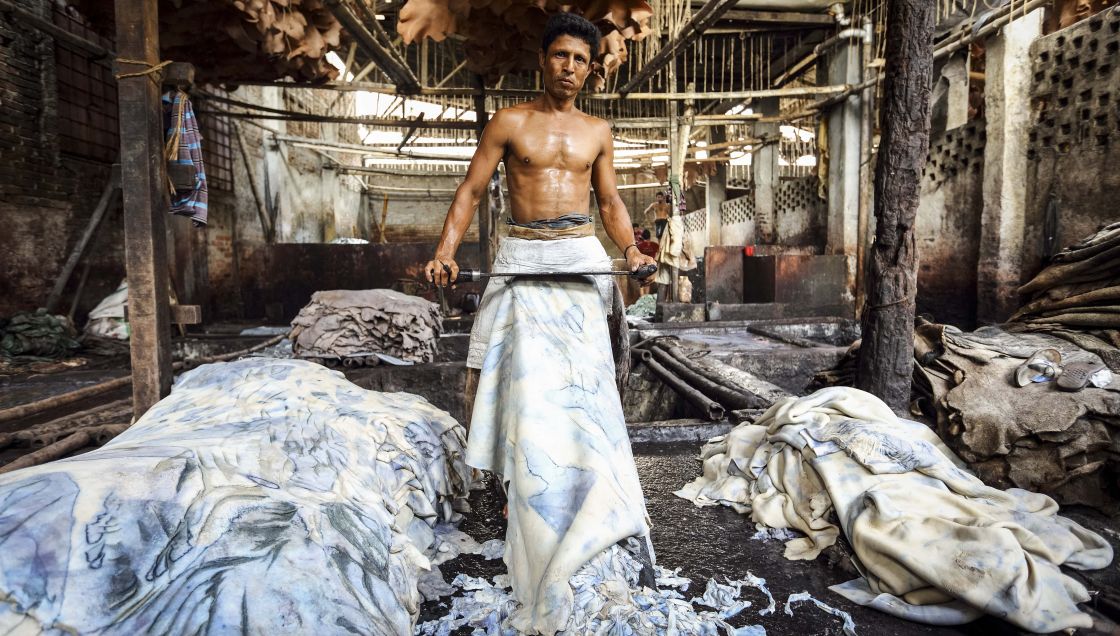 Ein Mann mit freiem Oberkörper gerbt ein großes Stück Leder mit einem großen Messer vor seinem Körper