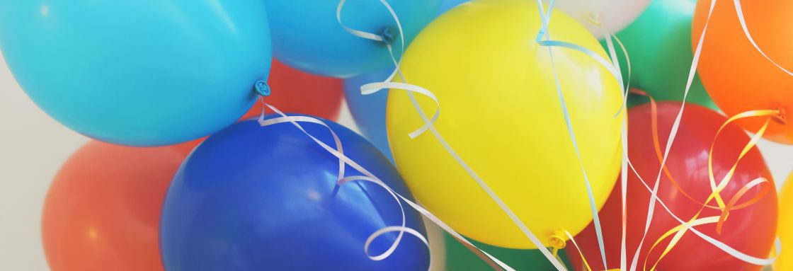 Eine Hand hält die Strippen von vielen bunten Luftballons.