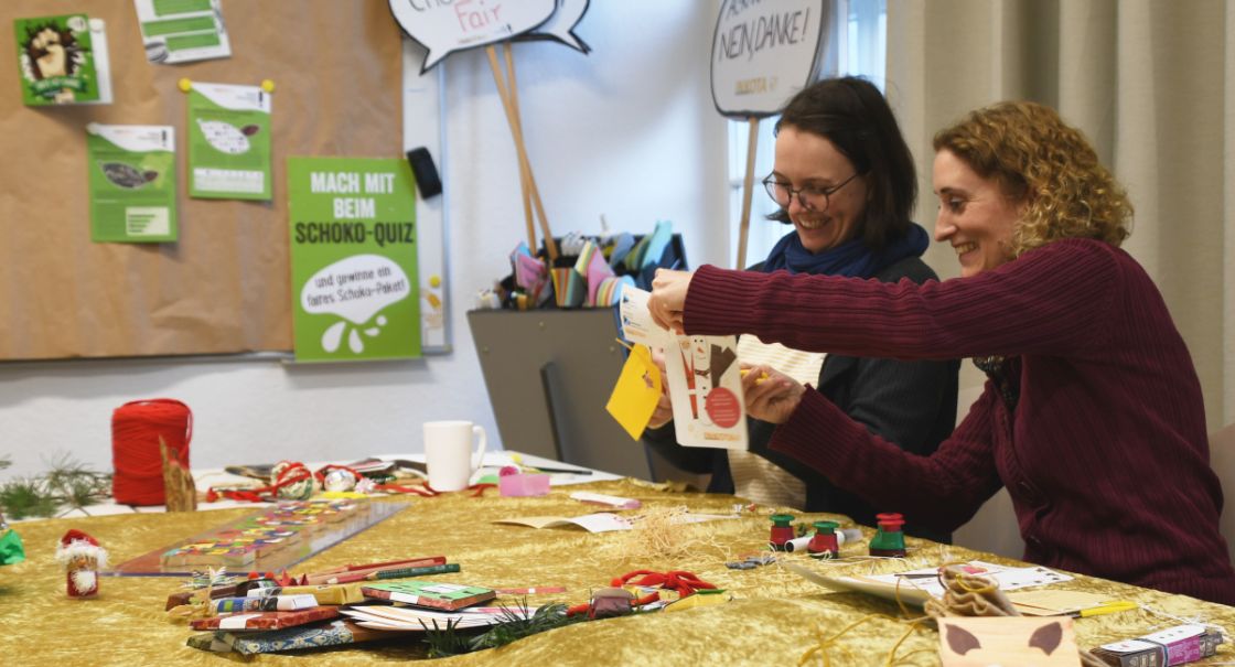 Aktion Faires Fest Ein Tisch mit vielen Bastelmaterialien und zwei Frauen