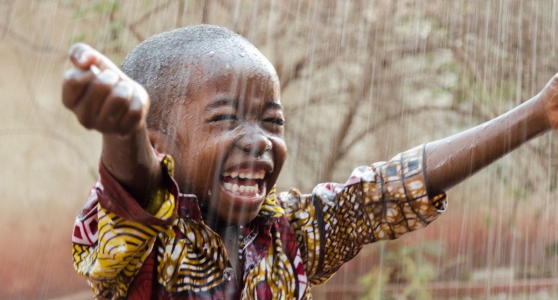 Ein Junge steht im Regen, breitet die Arme weit aus und freut sich sehr