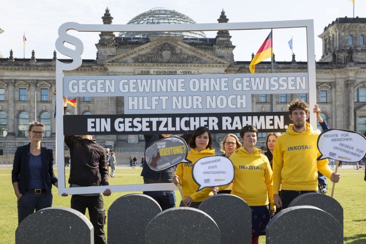 Eine Gruppe Mitarbeitende von Inkota stehen mit Protestschildern vor dem Reichstag in Berlin