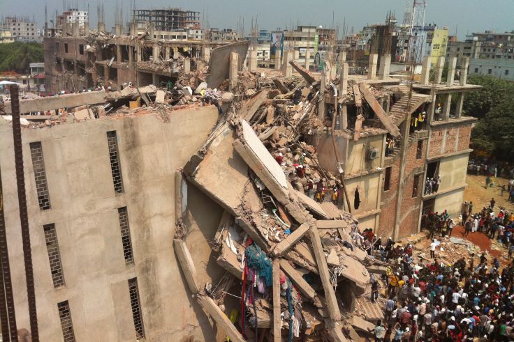 ein hohes Fabrikgebäude, was teilweise eingestürzt ist. Rettungskräfte sind in den Trümmern zu sehen