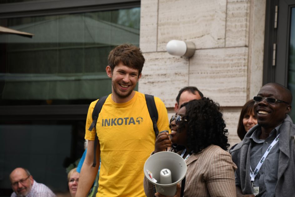 Ein junger Mann mit gelben T-Shirt lächelt eine Frau an, die in ein Megafon sprich