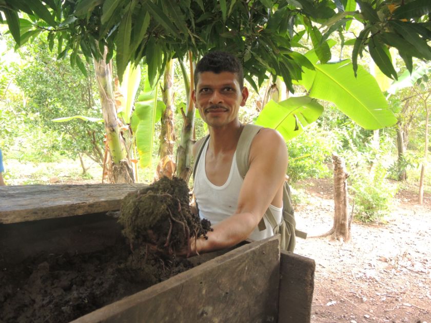 Ein Mann hält Kompost in seiner linken Hand und schaut lächelnd in die Kamera