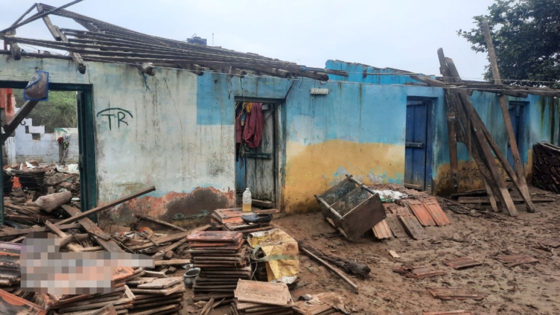 Ein entdachtes Haus mit blauer Außenwand vor dem Trümmer zu sehen sind