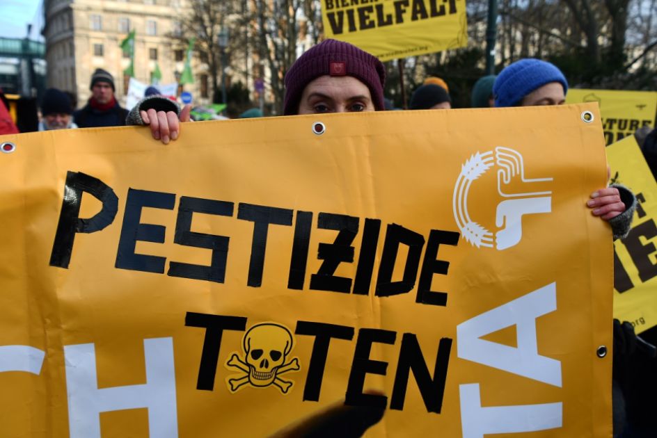 Frau schaut über ein Banner mit der Aufschrift Pestizide töten