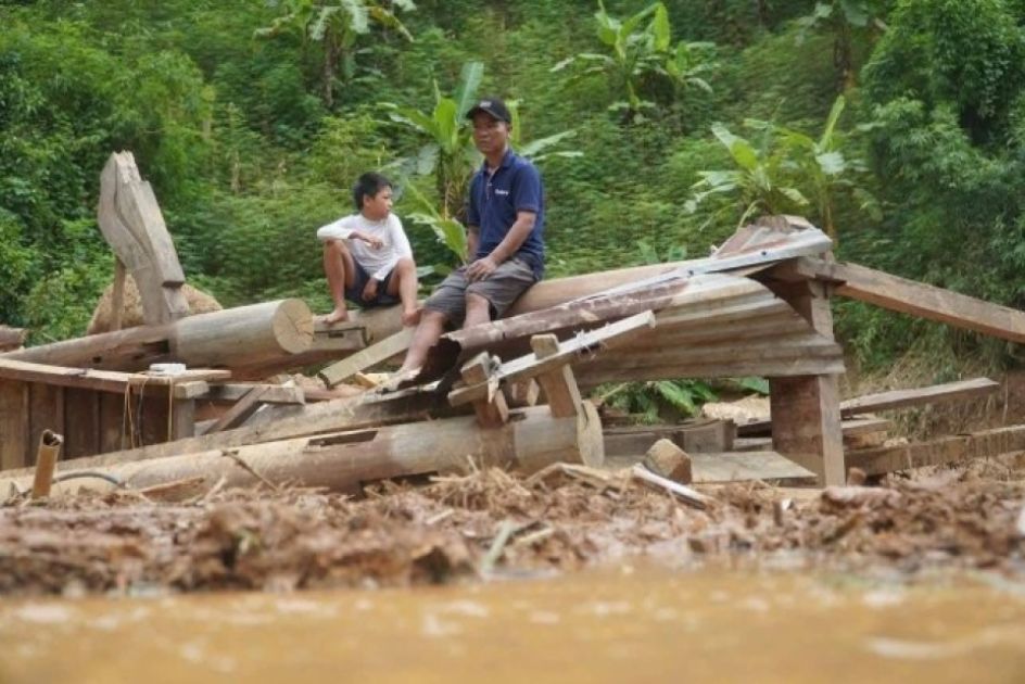 Ein Mann und ein Junge sitzen auf den Resten eines Hauses, davor Wasser