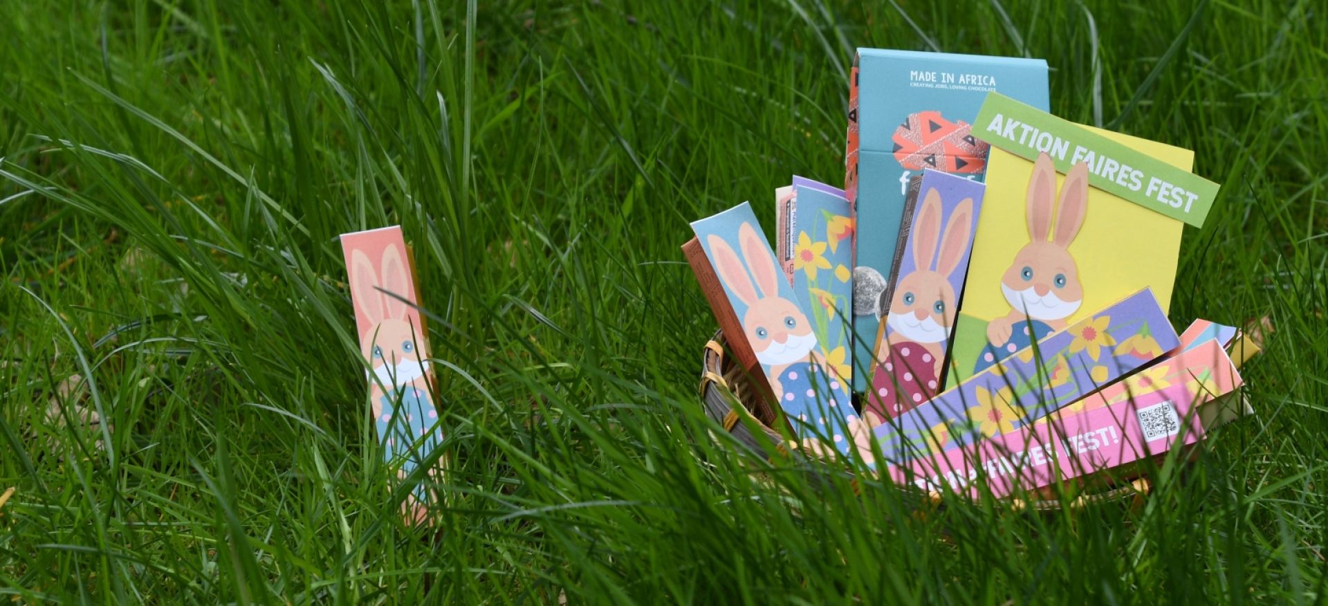 Osternest selber machen - damit es garantiert fair und bio ist! Ein Schokoriegel und ein Osternest mit Hasen- und Blumenbildern im Gras