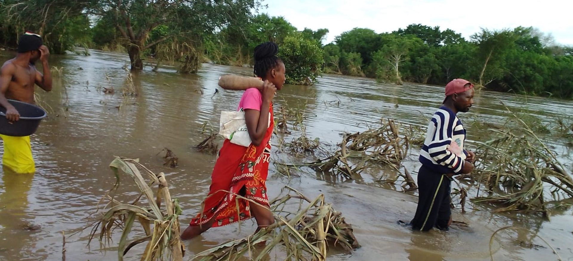 Menschen in Mosambik laufen knietief durch das Wasser eines überflutetetn Maisfeldes