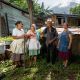 Drei Frauen und ein Mann mit Hut stehen in El Salvador vor einem Haus. Eine Frau hat eine Hacke in der Hand.