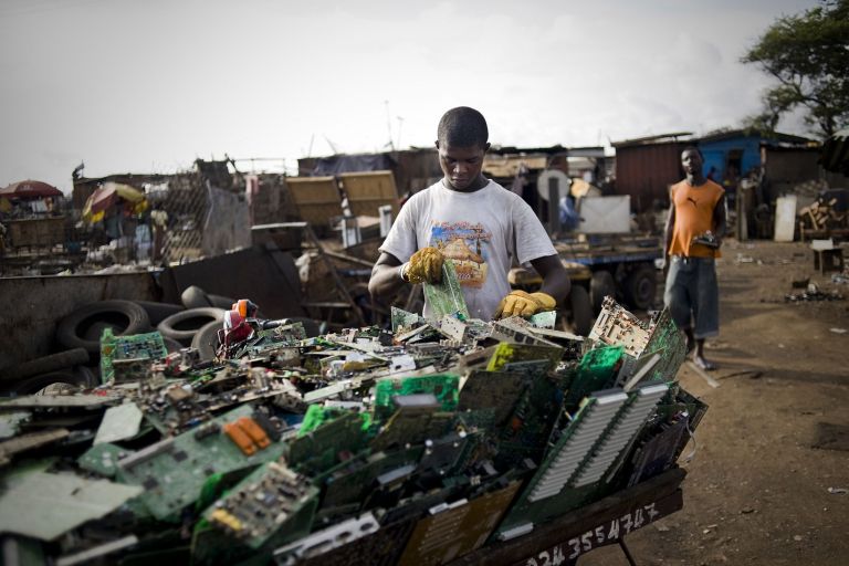 Schwarzer Mann sortiert Platinen und anderen Elektroschrott in einem Container