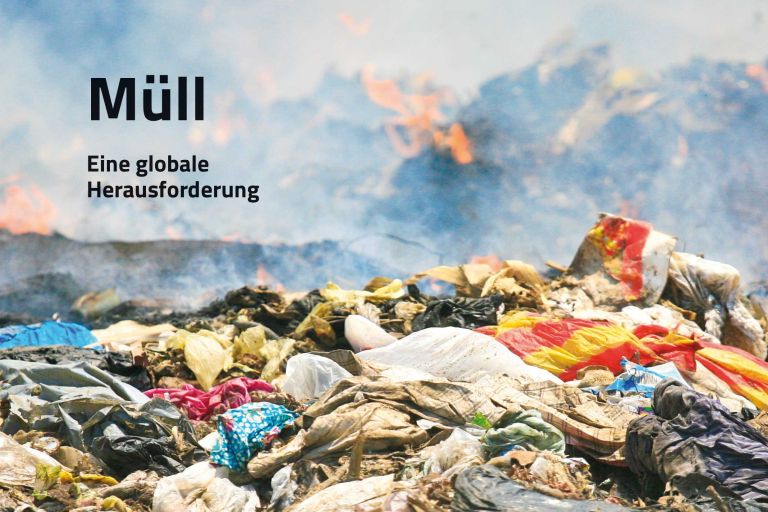 Ein großer Berg mit Plastikbeuteln, im Hintergrund brennt ein Müllberg