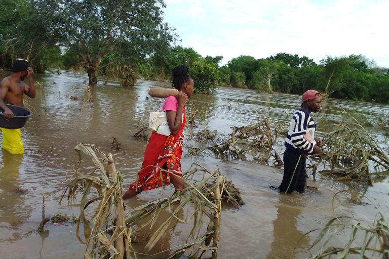 Menschen in Mosambik laufen knietief durch das Wasser eines überflutetetn Maisfeldes