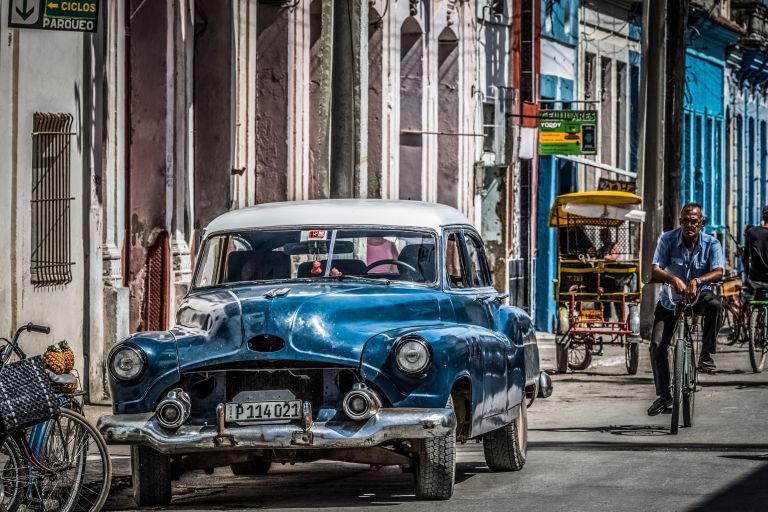 Eine Straßenszene in Kuba: ein Oldtimer und ein Mann auf dem Fahrrad