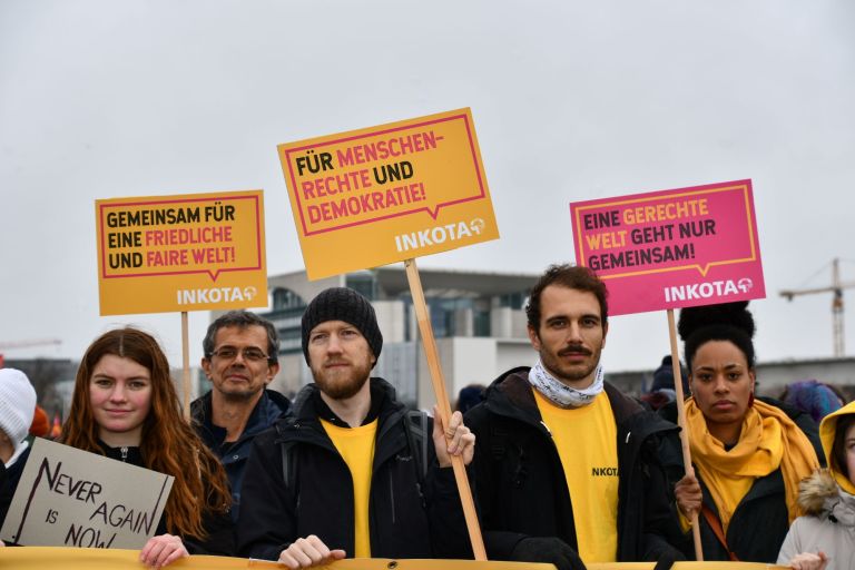 Eine Gruppe Menschen mit Schildern mit der Aufschrift "Gemeinsam für eine friedliche und faire Welt!", "Für Menschenrechte und Demokratie" und "Eine gerechte Welt geht nur gemeinsam, INKOTA" vor dem Kanzleramt