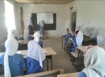 Mädchen mit weißen Kopftüchern in Rückansicht beim Schulunterricht in einem Klassenraum